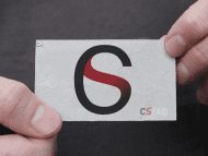 A visual from Carlos Simpson Design Studio featuring a bold, oversized 'CS' monogram in black and deep burgundy, symbolizing the brand’s identity. Framed like a product display, the image is held at the edges by two hands pointing inward — directing attention to the logo’s iconic form. Below the artwork, a tagline reads: “Passionately believe that strong, evocative digital content is the key to selling your product.” The design emphasizes the importance of branding, visual identity, typography, and digital marketing, reinforcing the studio’s core values: creativity, clarity, and strategic storytelling. Contact information at the bottom anchors the studio’s London-based presence and call to action.