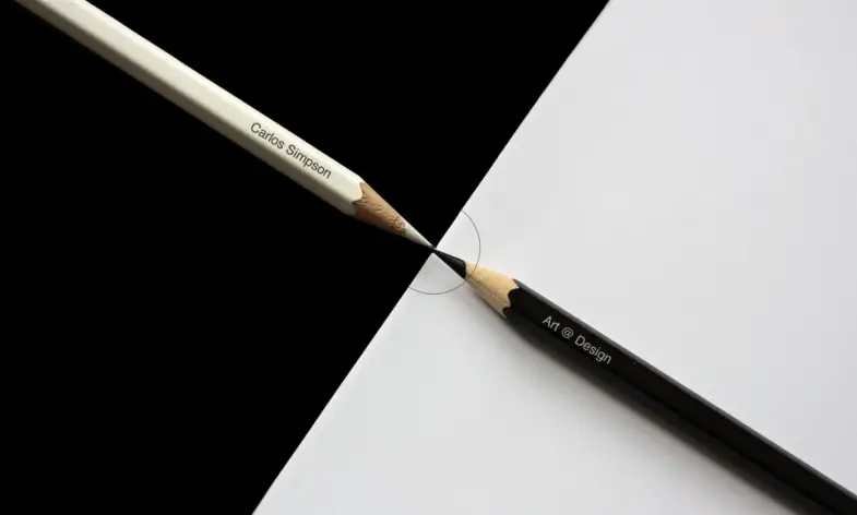 Two sharpened pencils - one white inscribed with “Carlos Simpson” and one black inscribed with “Art @ Design” — meet precisely at their tips, forming a perfect boundary between a black and white background. The image symbolizes balance, creativity, and the seamless integration of art and design. Representing Carlos Simpson Design Studio, the composition highlights core brand values: conceptual precision, minimalist beauty, and the powerful intersection of identity, contrast, and creative innovation.