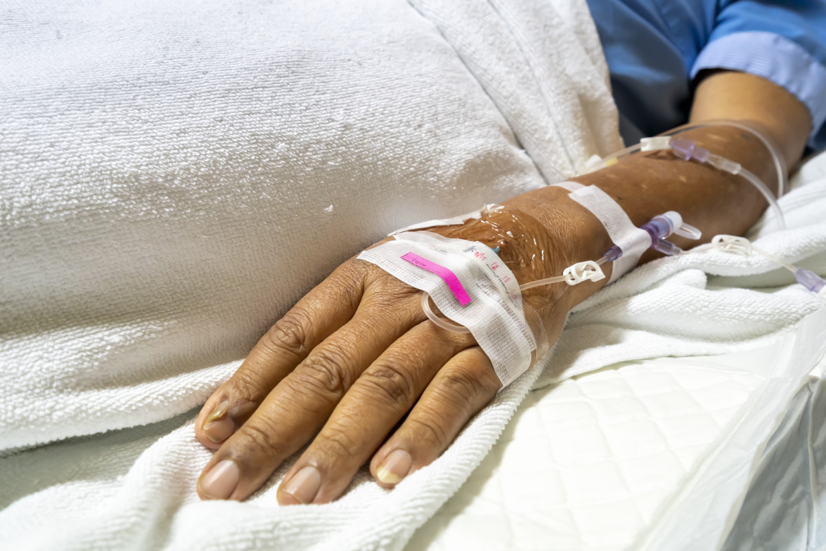 Selective focus on hand and drip tube of a patient or case in hospital ward lie on bed during dosing of intravenous saline solution medical and vitamin