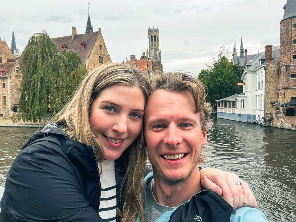 A couple traveling together stands in front of the canal in Brugge