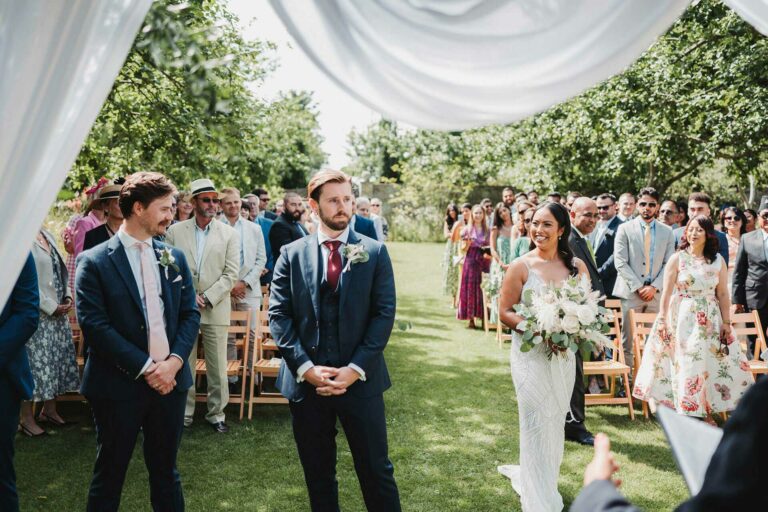 A groom waits for his bride at the outdoor ceremony in the wild apple orchard at Chapel House Estate