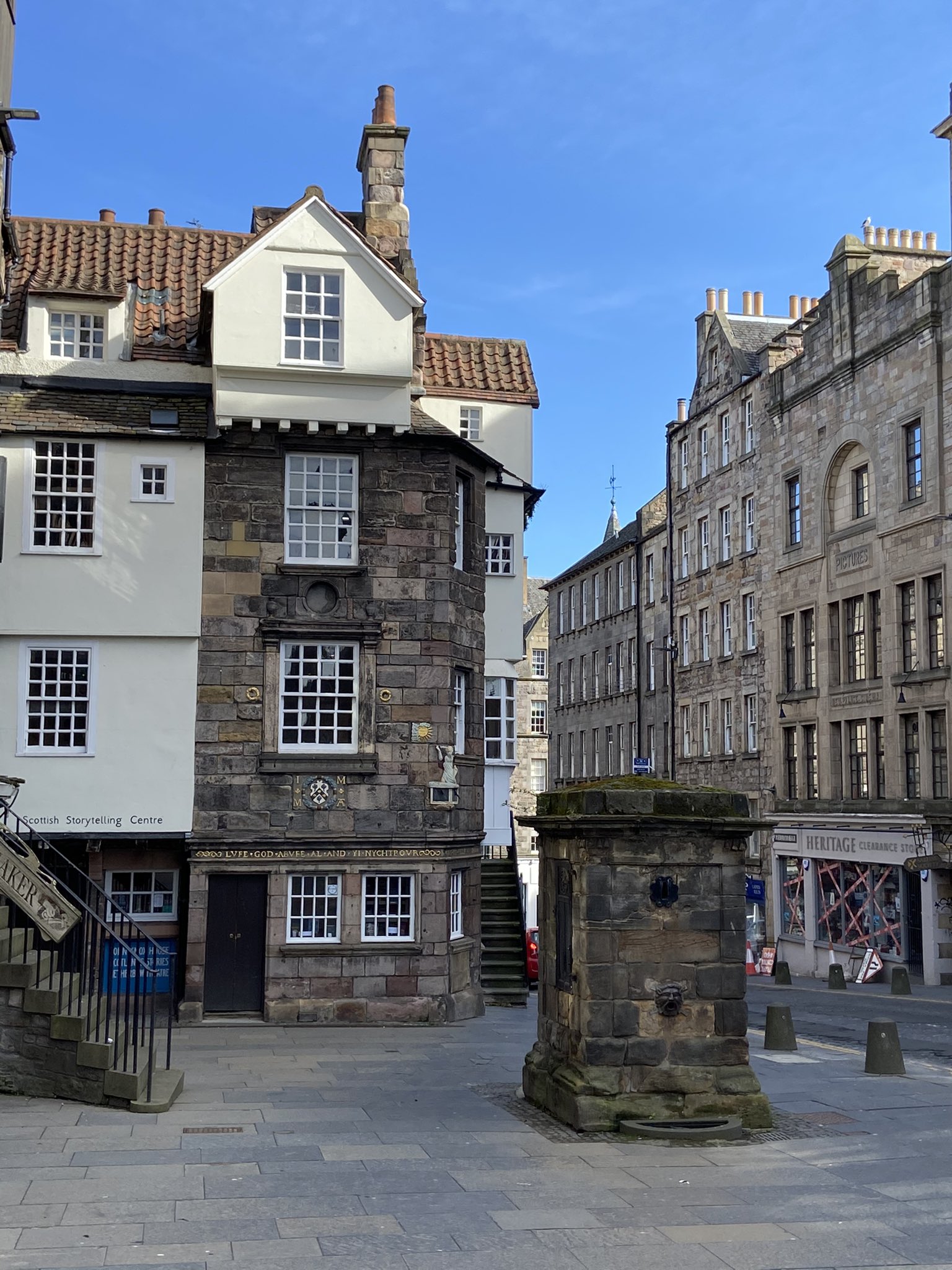 View of John Knox House from the Royal Mile on a sunny day, including the old water fountain on the pavement in front of it.