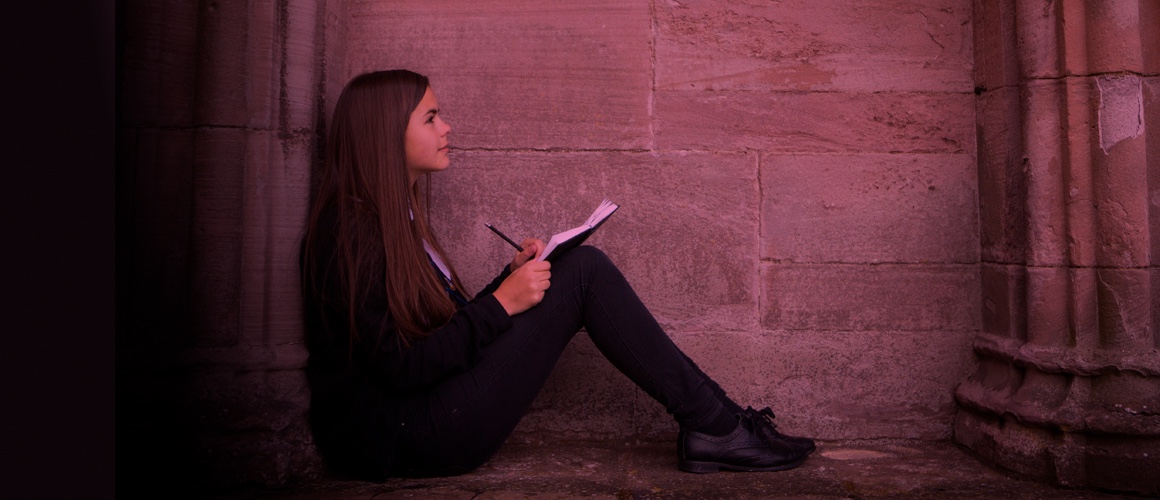 Girl writes story on pad of paper while sitting in a classical building