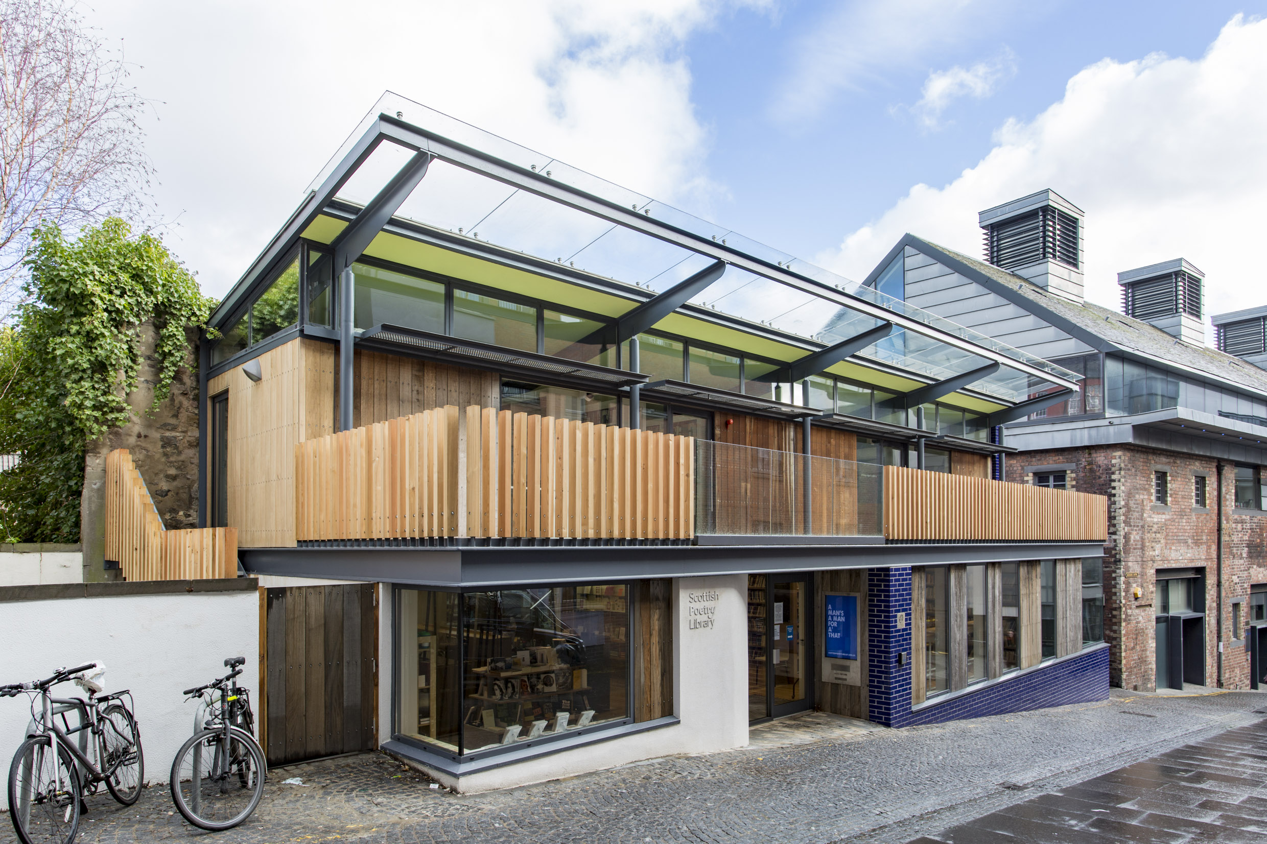 A photo of the Scottish Poetry Library, a modern building with large glass windows, a glass roof and a wooden slatted balcony.