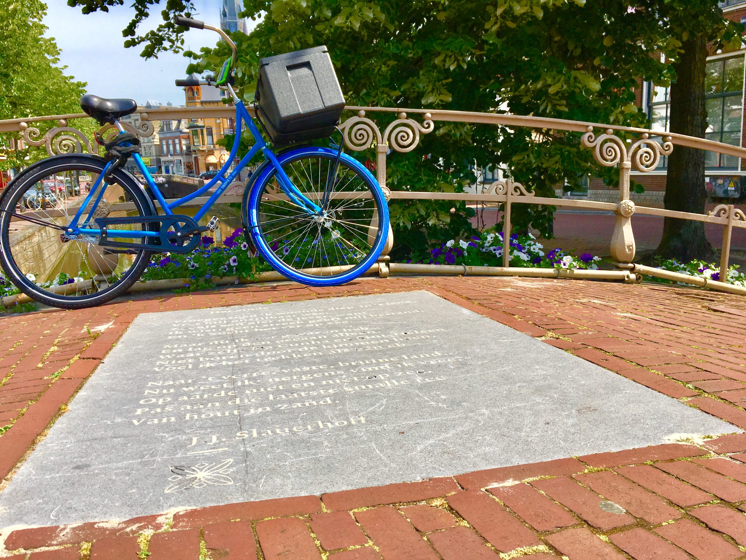 A blue bike leans against the metal railings of a curved stone bridge. A Poem in engraved in one of the bridge's flagstones.