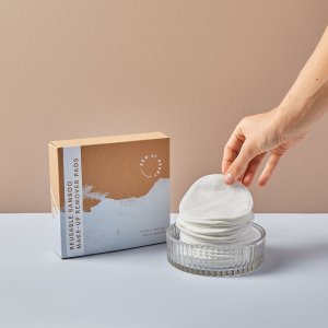 Hand reaching in for a zero-waste make-up remover pad with packaging in background