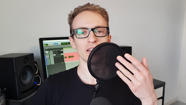 joe holding a pop filter sitting in front of computer