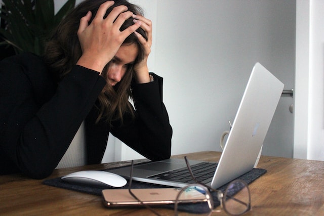 woman with head in hands with laptop on desk