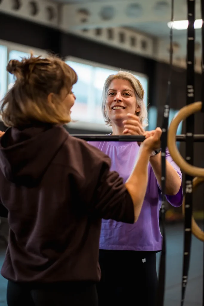 De coach begeleidt een vrouwelijk lid tijdens een fundamentals-les, waar ze in small group setting de basisprincipes van CrossFit leert met professionele coaching.