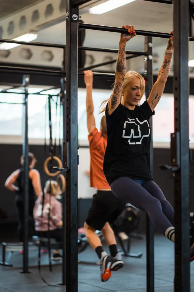 Een lid voert een kipping pull-up uit aan een optrekstang tijdens een small group CrossFit-les. Met verschillende leden op de achtergrond.