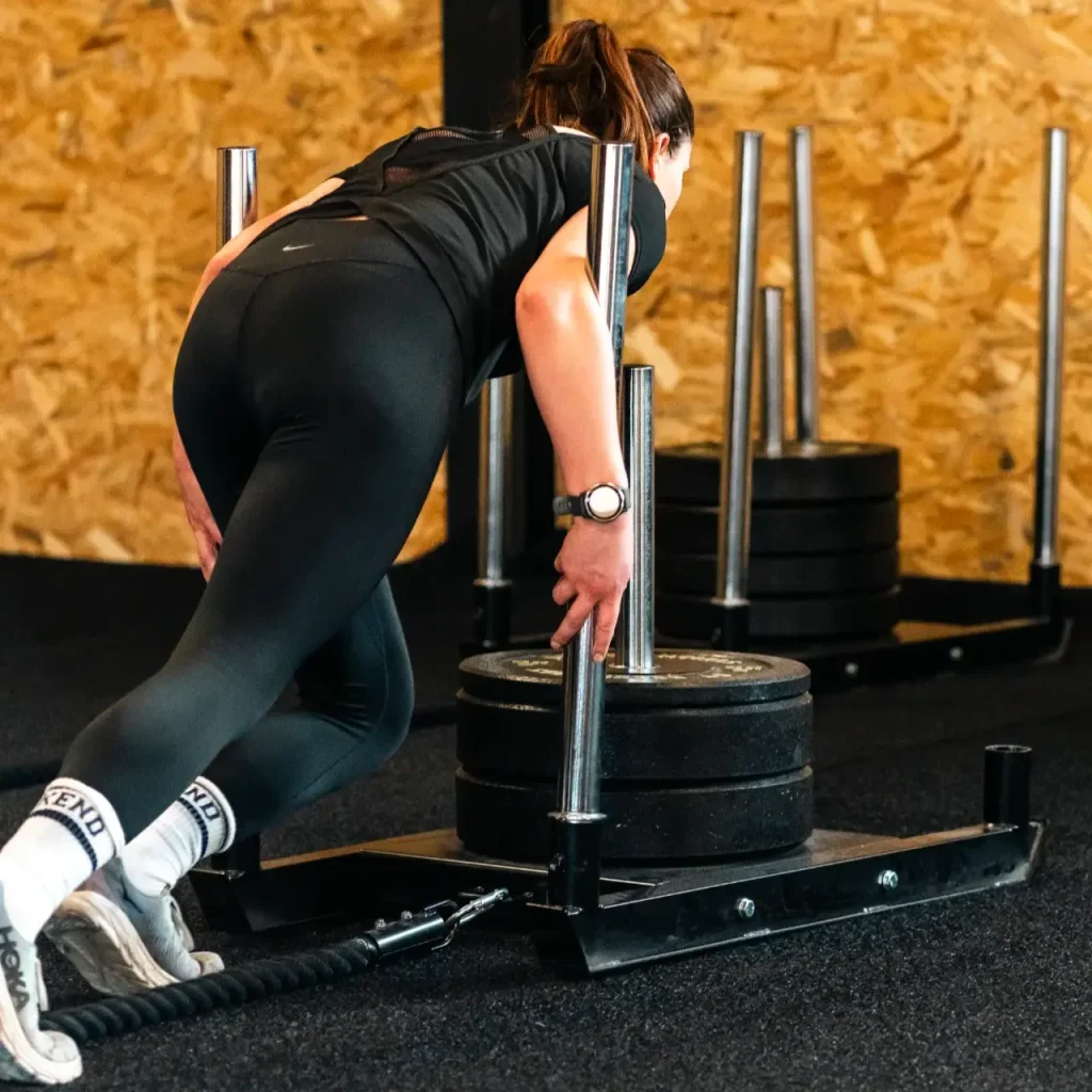 Een sportieve vrouw duwt een slee over het gras tijdens de HYROX-les.