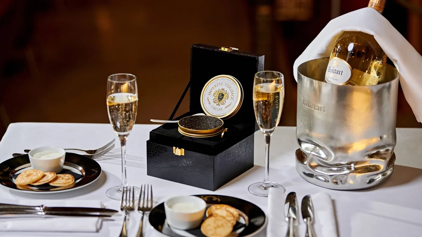 Een geopend blikje kaviaar in een zwart geschenkkoffertje op een restauranttafel met champagne en blini’s