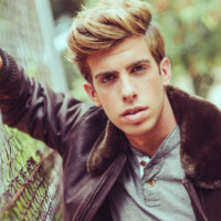 Portrait of a young handsome man, model of fashion, with modern hairstyle in urban background wearing aviator leather jacket. Blonde hair
