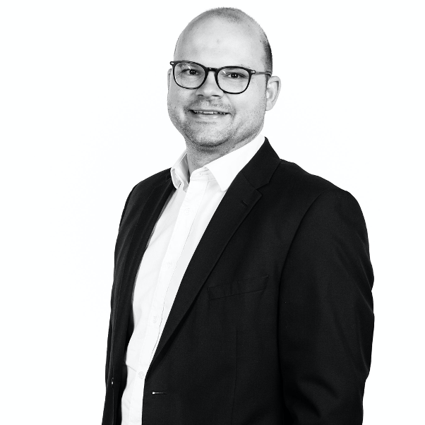 Black and white headshot of Sam Chown wearing a white shirt and dark jacket.