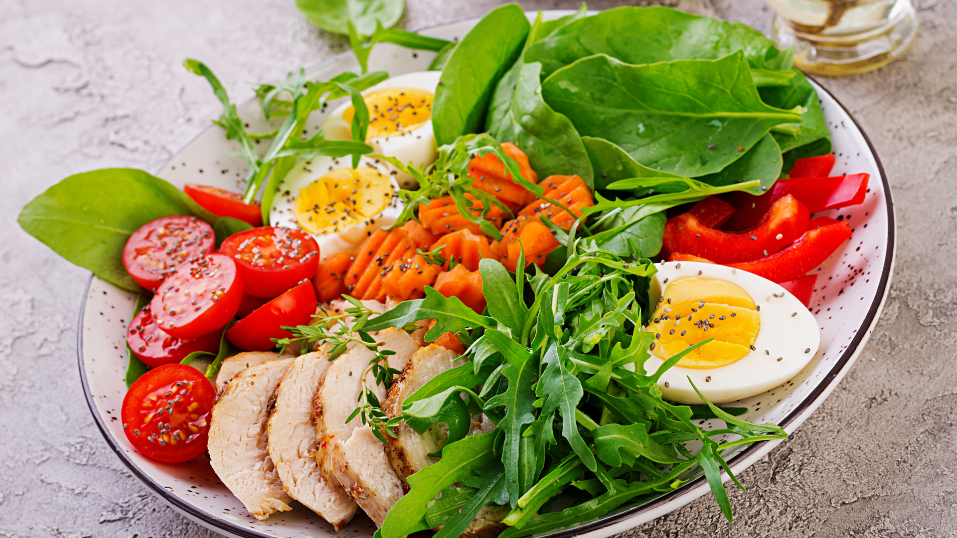 En nærbilde av en sunn matrett med cherrytomater, gulrøtter, ruccola, spinat, paprika, kokt egg og kyllingfilet – ideell for hjertevennlig kosthold