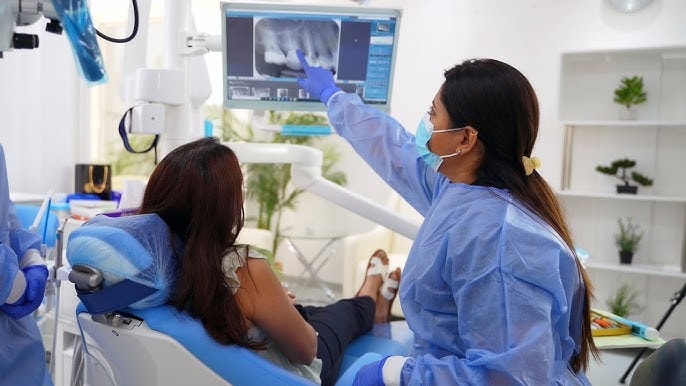 Digital tannbehandling: Den beste løsningen for et perfekt smil 2 En tannlege peker på et røntgenbilde på skjermen mens en pasient slapper av i tannlegestolen og ser på skjermen.