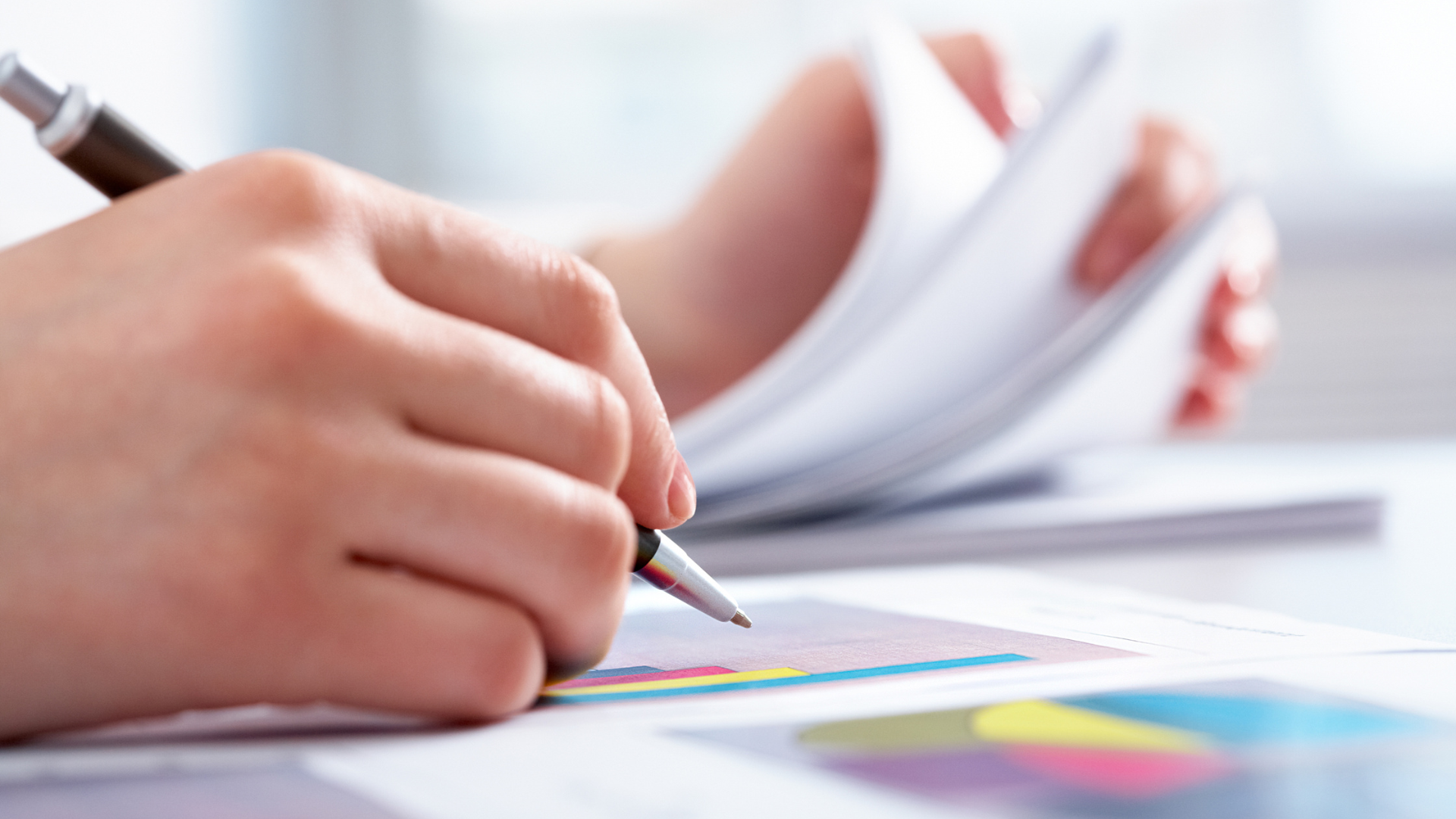 Hånd som fyller ut skjema med fargerike grafer og dokumenter – symboliserer refusjon for tannbehandling