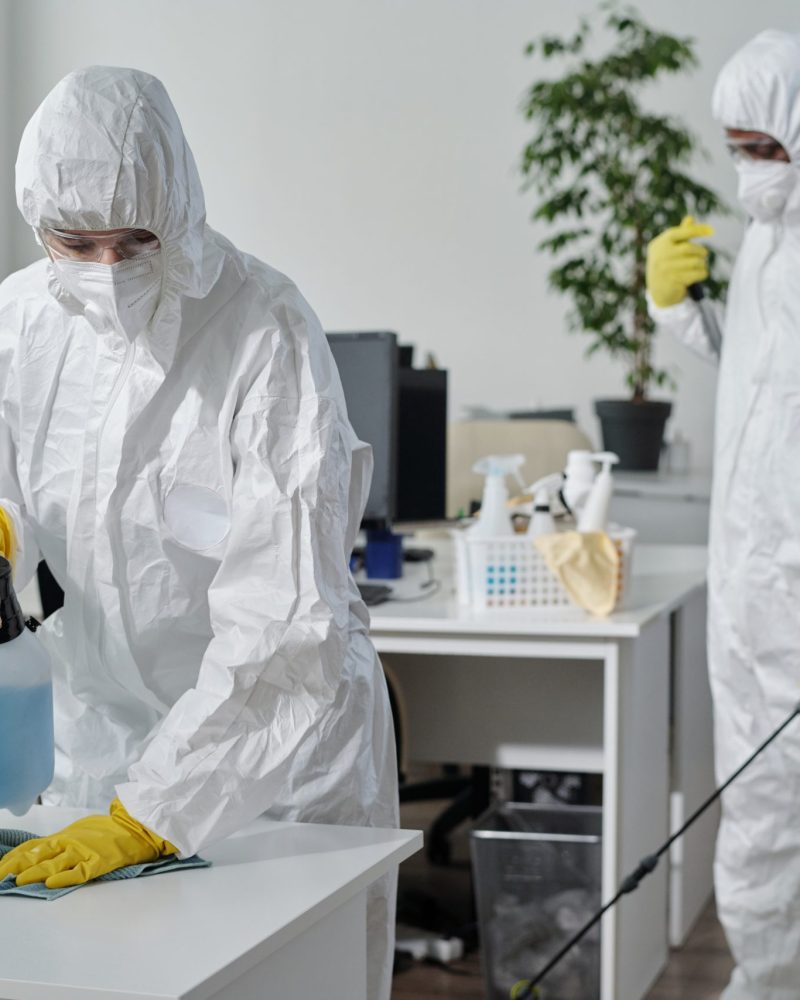 Contemporary disinfection service company staff in protective workwear Contemporary disinfection service company staff in protective workwear carrying out their work in spacious openspace office