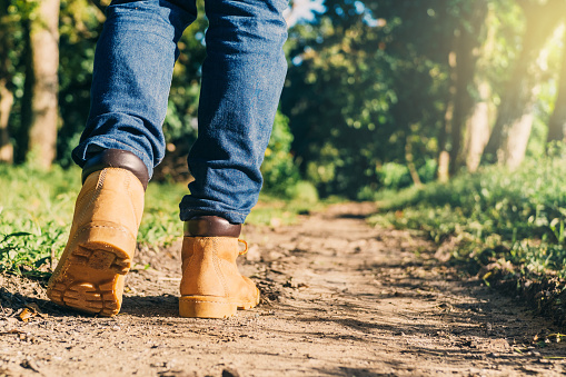 feet of an adult wearing boots to travel walking in a green forest. travel nature and hiking concept.