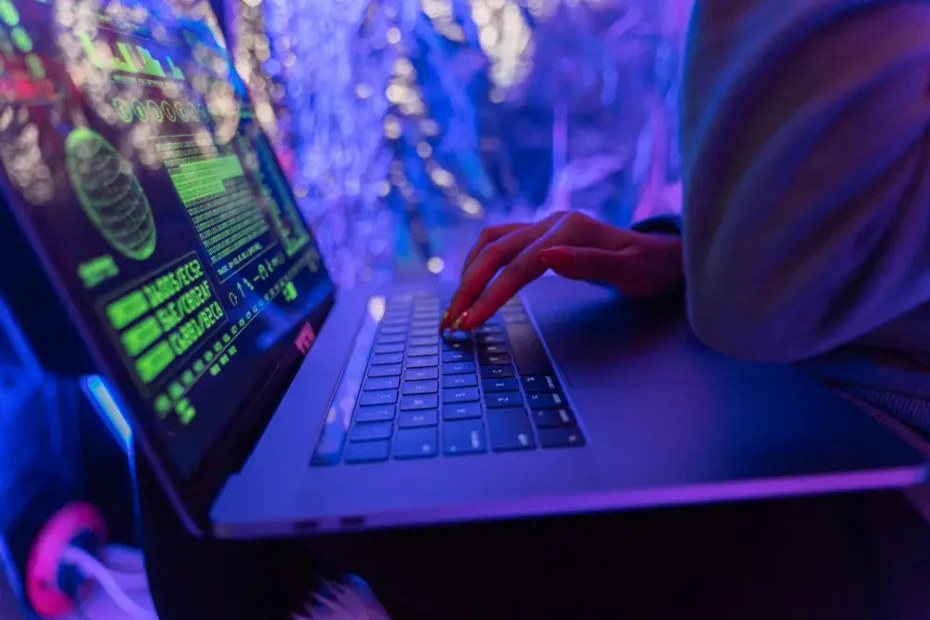 Main tapant sur un clavier d'ordinateur avec des écrans affichant du code, ambiance cybersécurité