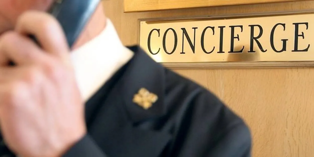 Les Clefs d'Or Hotel concierge in uniform speaking on phone near "CONCIERGE" sign with fleur-de-lis emblem