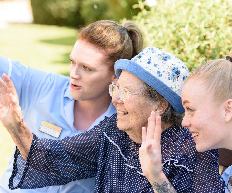 An elderly resident smiling with two members of staff in the garden