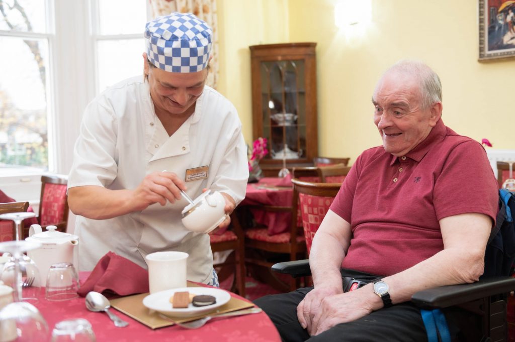 Elderly resident being poured a cup of tea by kitchen member of staff