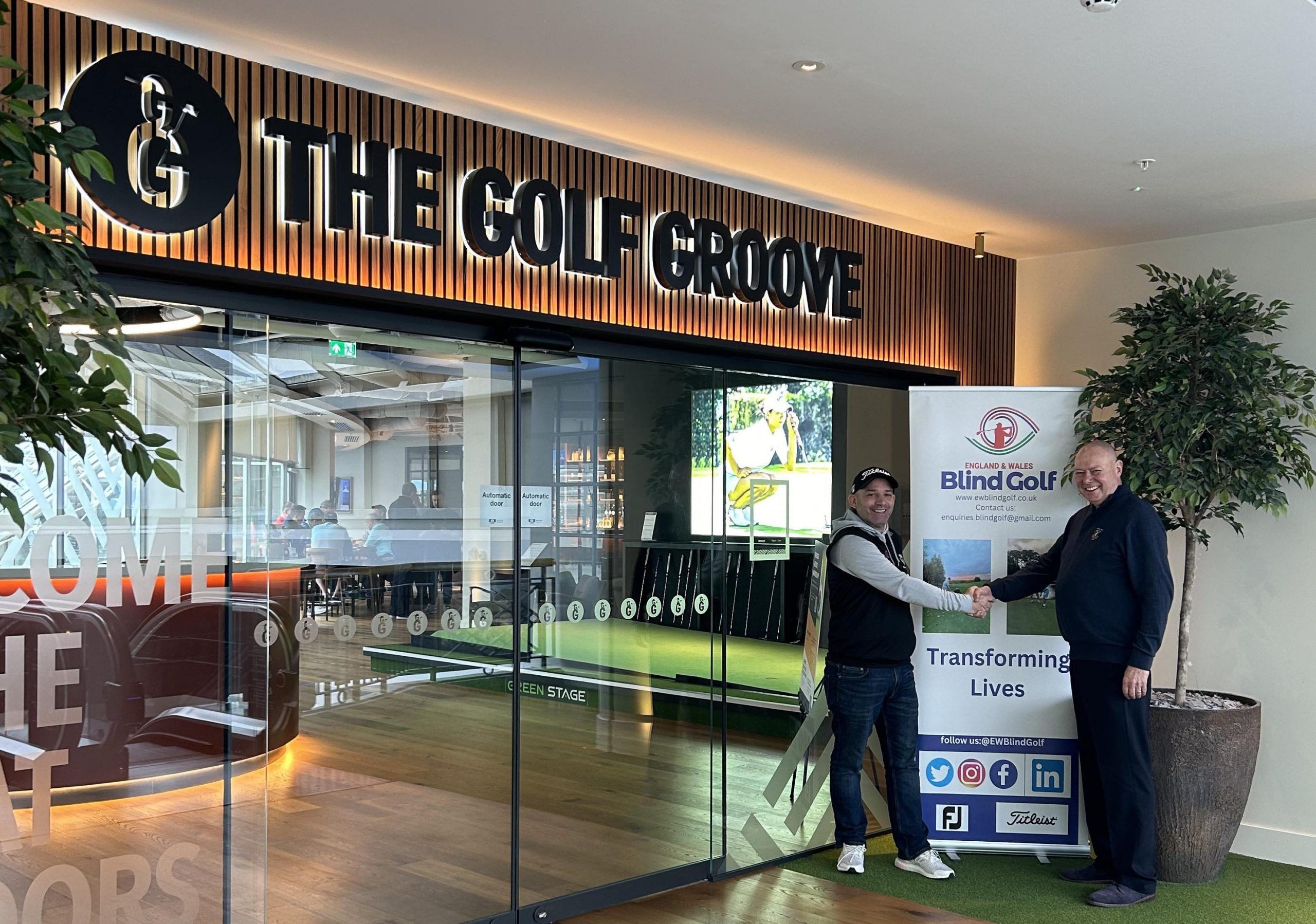 Photo show Andy Gilford and David on the right hand side. They are standing in front go and EWBG Banner and glass doors with Golf Groove written above the doors.