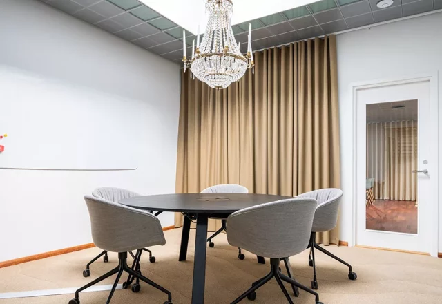 Konferensrum med runt bord, grå stolar och kristallkrona