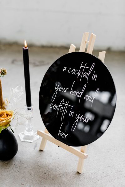 welkomsbord lets celebrate plexiglas zwart schildersezel huren bruiloft rond bord witte letters kalligrafie a cocktail in your hand