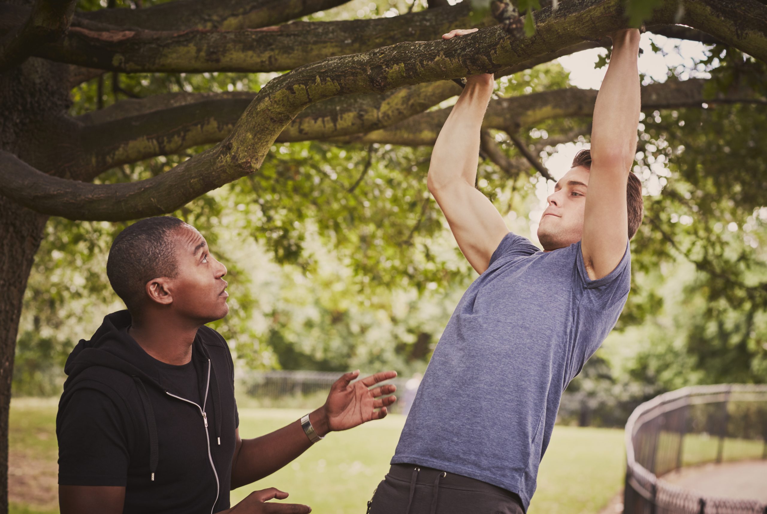 Personal trainer instructing man on pull ups using park tree branch
