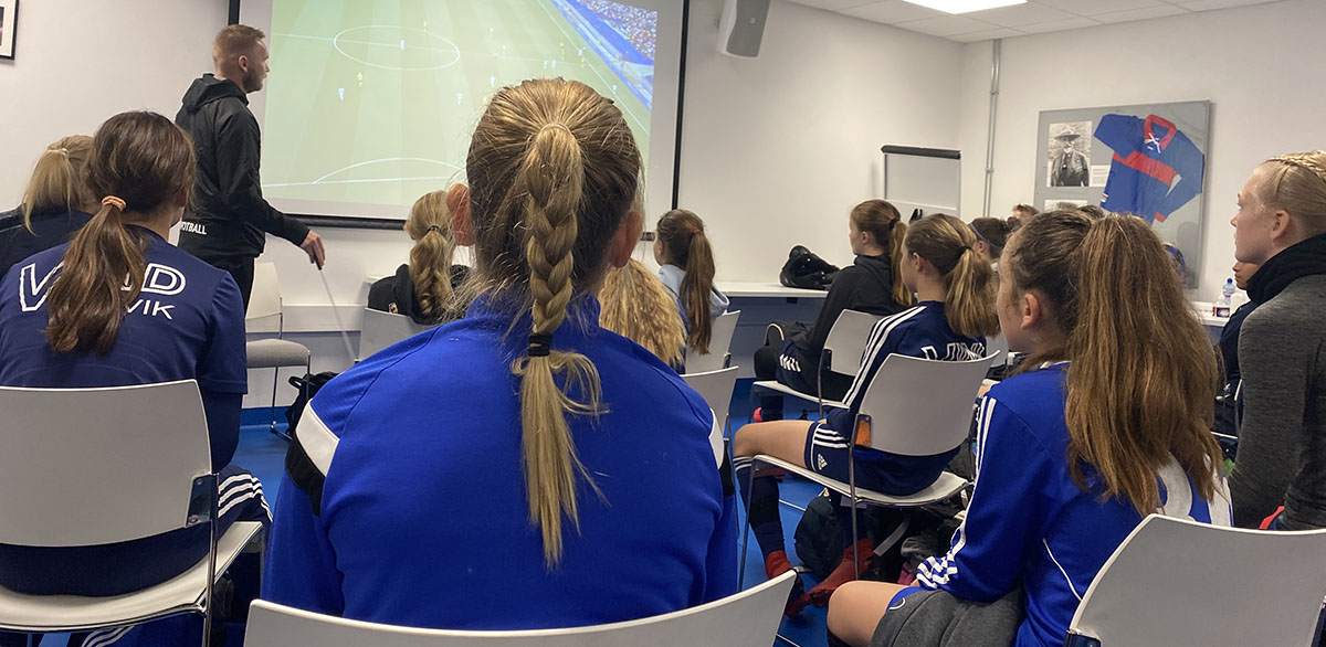 Bilde som viser jentespillere fra Hasle-Løren og andre samarbeidsklubber med Vålerenga på en videoanalyse før trening.