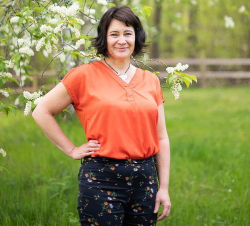 Susanne Sabith - Din Framstegscoach - står framför en häggbuske och utstrålar glädje och energi.