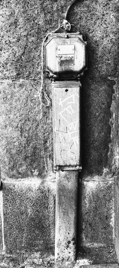 Bild: svartvitt foto på en stengrund till ett hus, eldosor med graffiti, en kabel och ett snöre bundet vid.