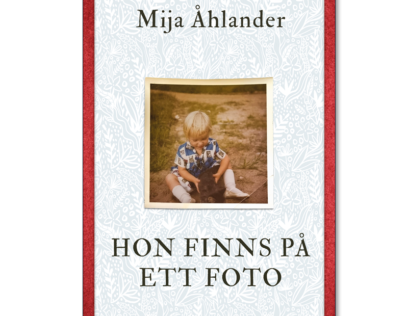 Omslaget till 'Hon finns på ett foto' av Mija Åhlander, vitt med röda kanter och ett foto av ett barn
