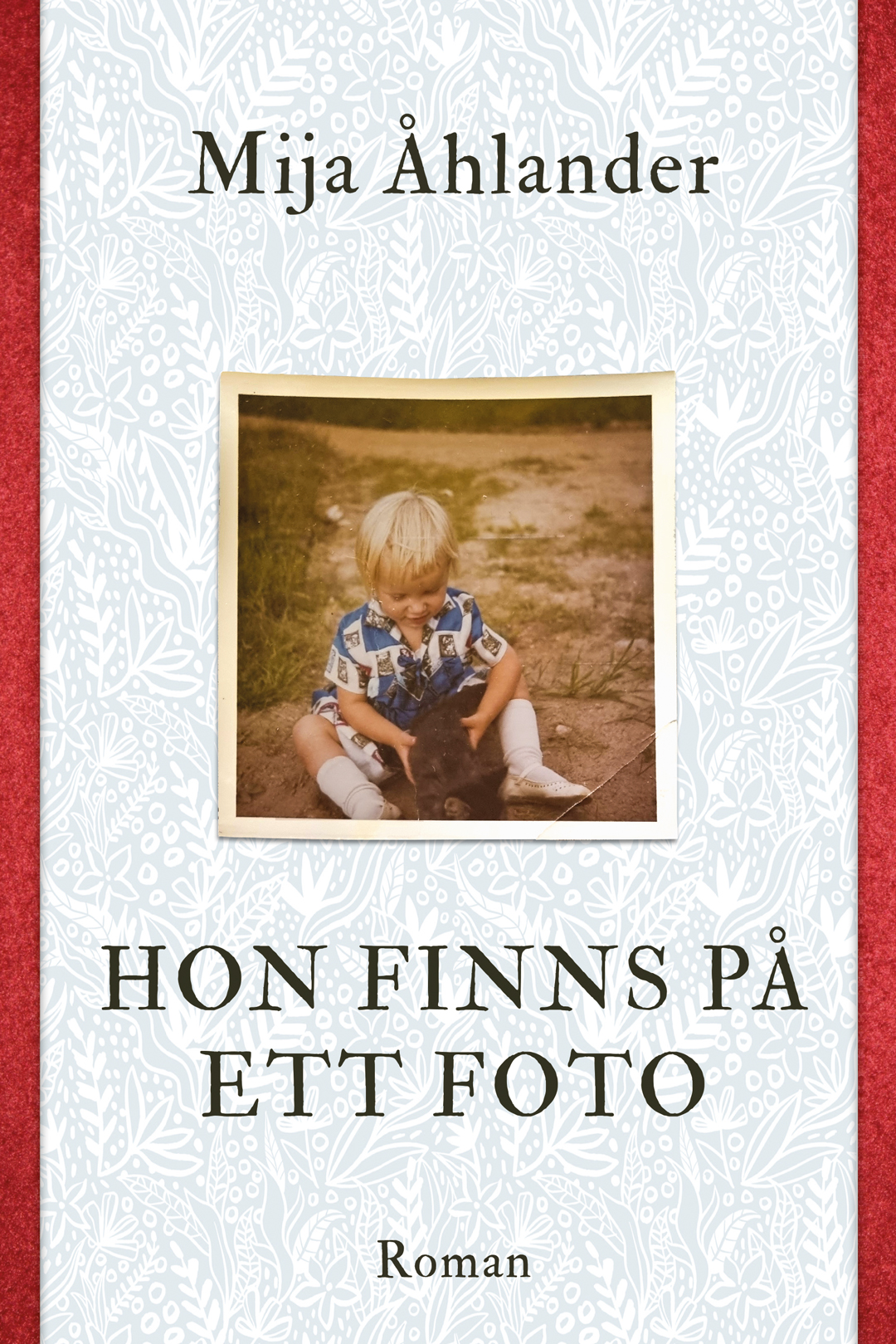 Omslaget till 'Hon finns på ett foto' av Mija Åhlander, vitt med röda kanter och ett foto av ett barn Omslaget till 'Hon finns på ett foto' av Mija Åhlander, vitt med röda kanter och ett foto av ett barn