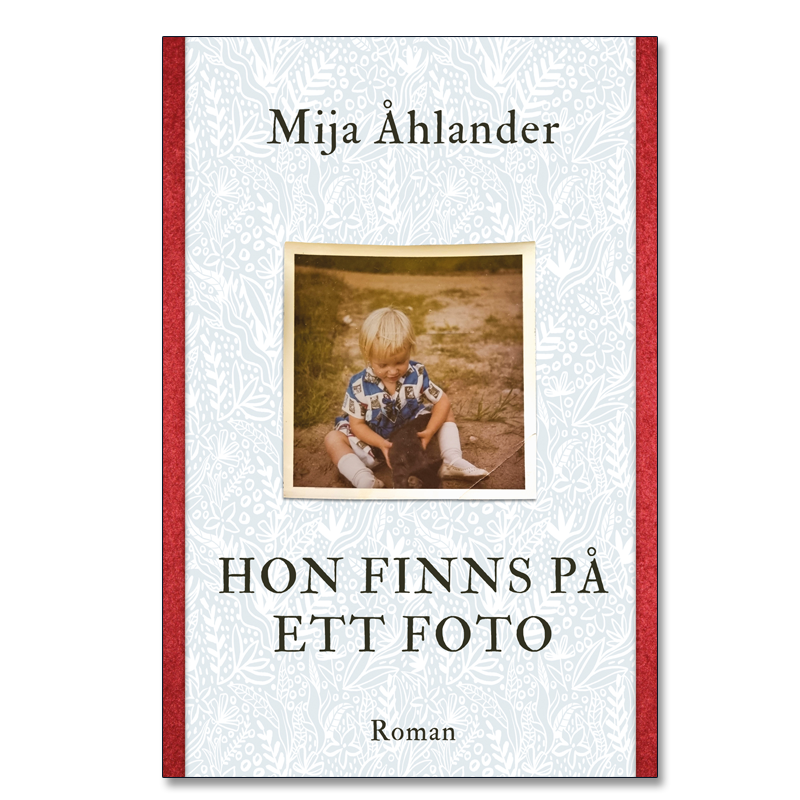 Omslaget till 'Hon finns på ett foto' av Mija Åhlander, vitt med röda kanter och ett foto av ett barn