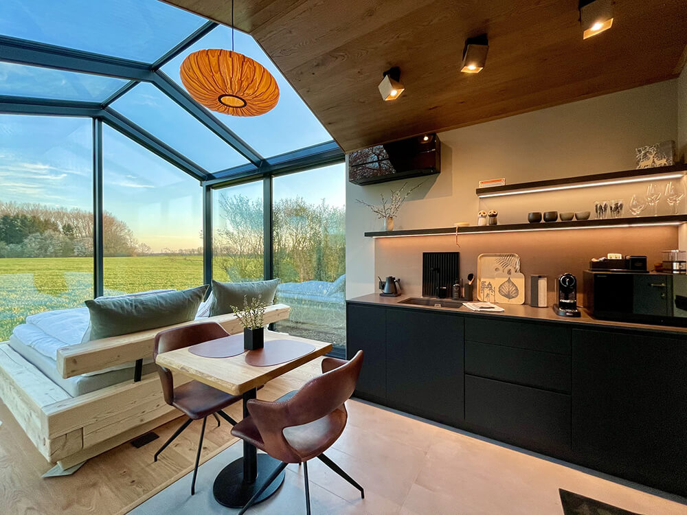 Udsigt til solnedgang gennem glasfacaden til mark og skov, et levende panorama hos Glashytterne