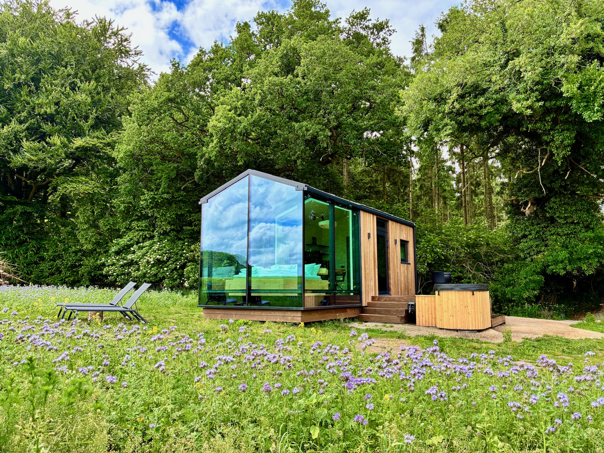 Glass Hut Lysa at dusk in a wildflower field with lounge chairs outside
