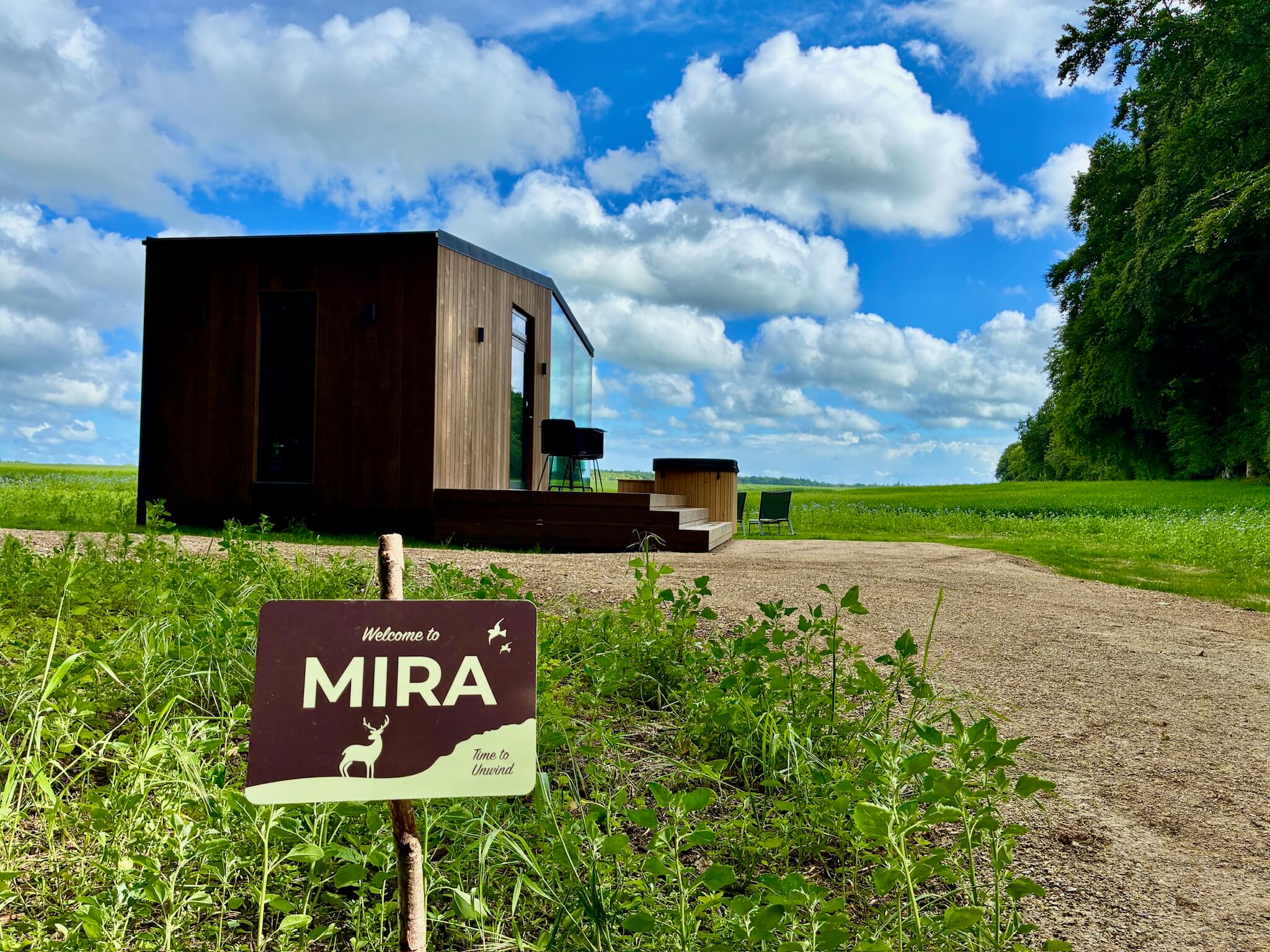 Glashytten Mira med indgangsskilt i en blomstereng