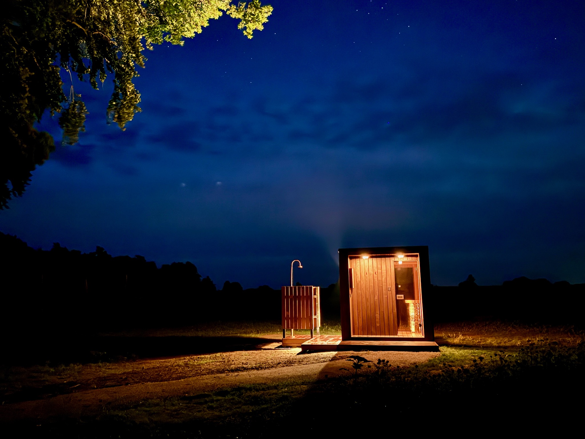 Outdoor sauna and shower lit up at night near Glass Hut Mira