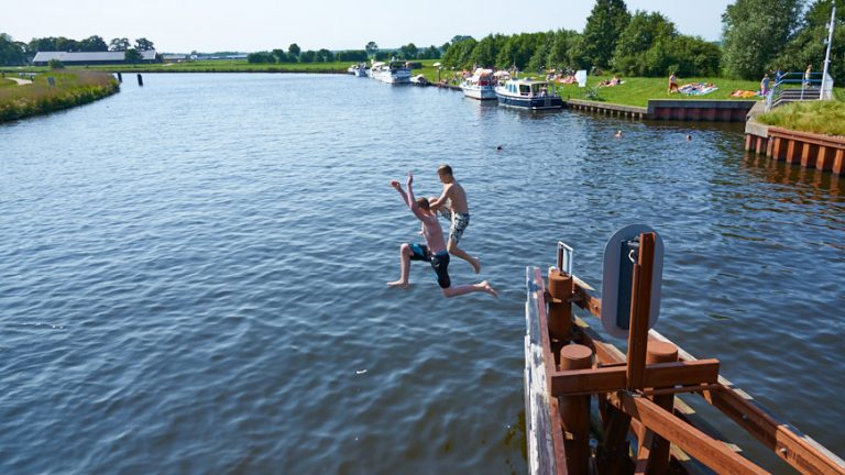 Twee jongens springen van brug in het water van de Eem