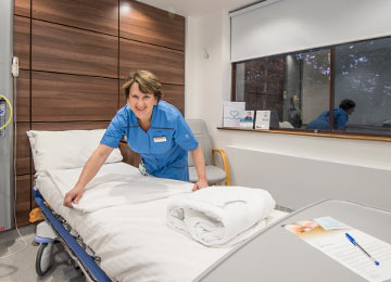 This photo shows a caring team member preparing a bed in a private room ready for the next hernia patient. They are smiling.