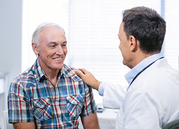 This photo represents a groin hernia patient being reassured by a medical professional, whose hand rests on the patient's shoulder.