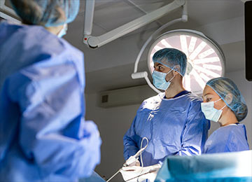 The photo shows an operating theatre with three surgical team operating a camera as a part of laparoscopic hernia surgery.