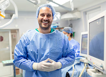Photo shows a delighted consultant surgeon with an operating theatre in the background.
