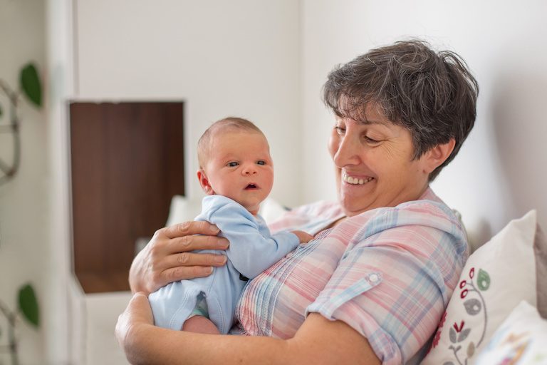 Beautiful baby boy in grandmothers arms at home