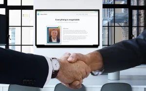 To personer i dress håndhilser i et lyst kontormiljø. I bakgrunnen vises en stor skjerm som viser nettsiden “Open Mind” med teksten “Everything is negotiable” og et portrett av nettstedets eier.