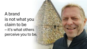 Smiling man standing in front of a small building made of round stones. On the left side, over a white gradient, is the quote: 'A brand is not what you claim to be – it's what others perceive you to be.