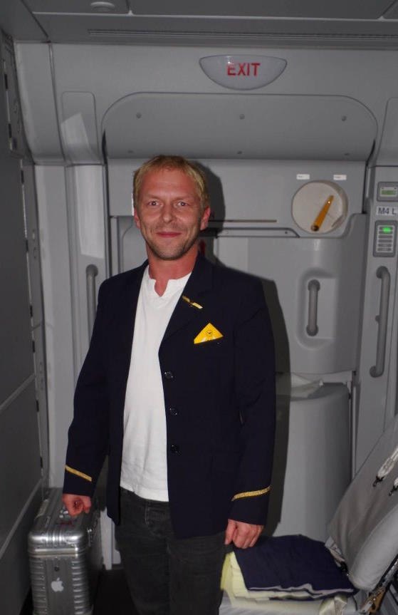 Person som poserer i flyvertuniform foran nødutgangen i et fly, under en flyreise ombord i en Airbus A380.
